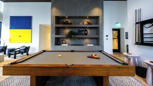 A billiards table with balls and cues, a seating area with chairs, and a wall with a blue and yellow artwork. - District 3704 (Miami)