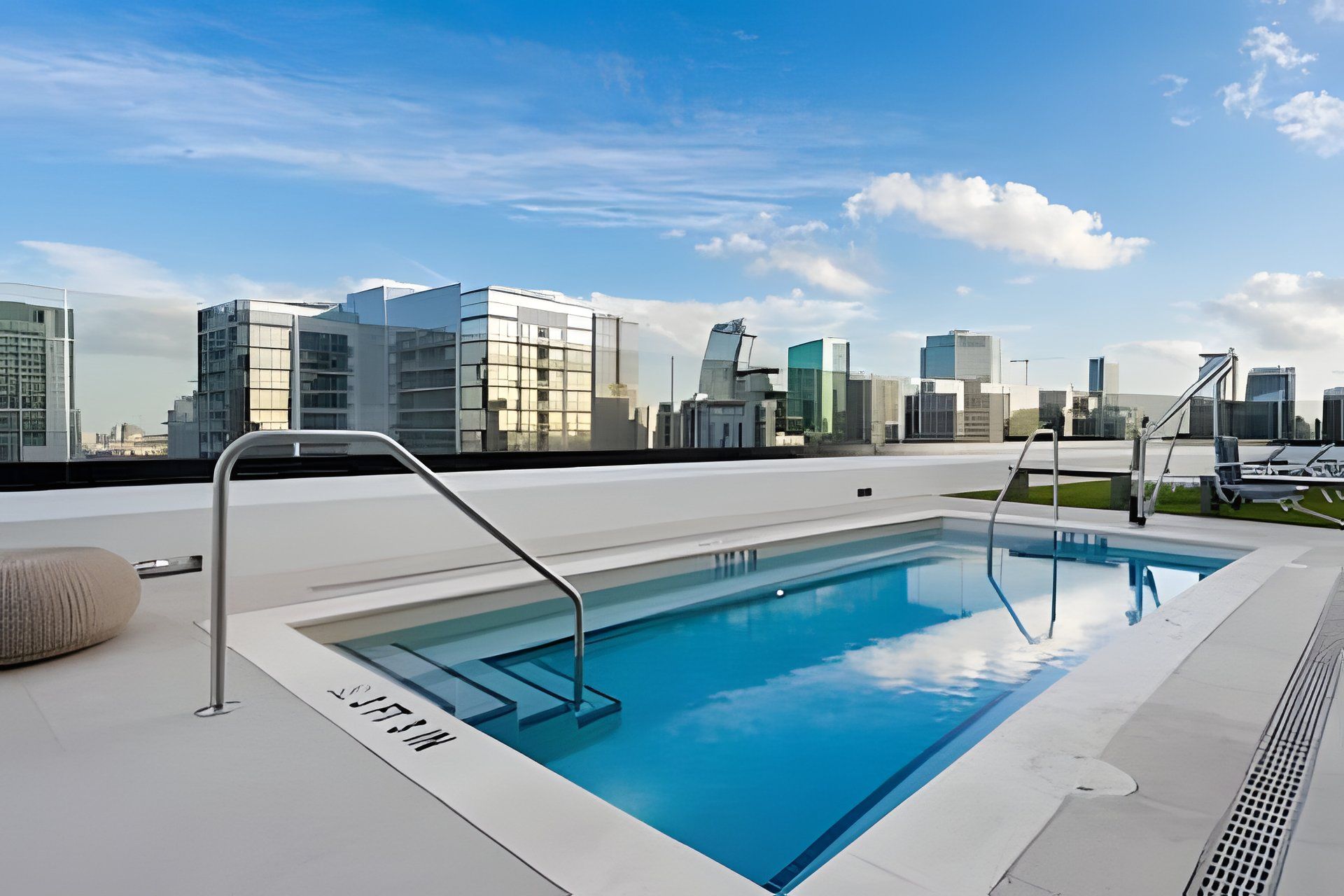 Una piscina en la azotea con vistas a un horizonte urbano, un área de descanso con asientos y un diseño arquitectónico moderno.