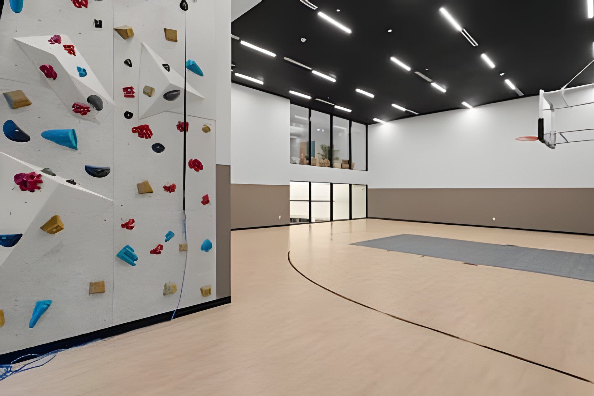 Un mur d’escalade équipé de différentes prises et un panier de basketball dans un grand espace intérieur.