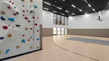 Un mur d’escalade équipé de différentes prises et un panier de basketball dans un grand espace intérieur.