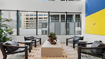 Ein modernes Interieur mit einer Sitzecke, einem zentralen Tisch und großen Fenstern, die Blick auf die Stadt bieten.