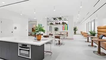 A modern kitchen with a central island, dining area with chairs and tables, and a bar area with plants.