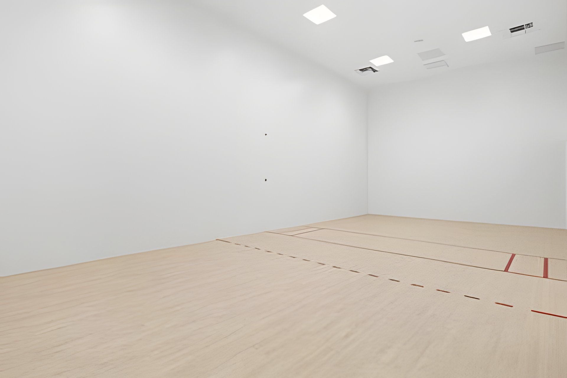 A spacious room with a wooden floor and white walls, featuring recessed ceiling lights.