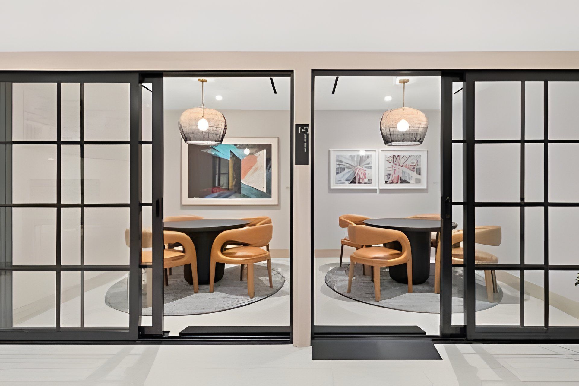 A room with a glass partition, a round table with chairs, and artwork on the walls.