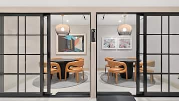 A room with a glass partition, a round table with chairs, and artwork on the walls.