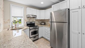 A kitchen with white cabinets, a stainless steel refrigerator, a stove, and a microwave. - Beach Block Brigantine Condo | Steps to Sand (Brigantine)