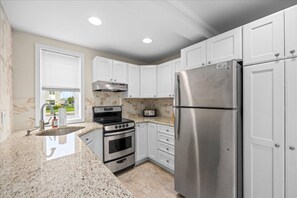 A kitchen with white cabinets, a stainless steel refrigerator, a stove, and a microwave. - Beach Block Brigantine Condo | Steps to Sand (Brigantine)
