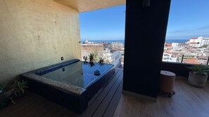A balcony with a hot tub, potted plants, and a view of a cityscape. - Fabulous Penthouse with Ocean & Mountain Views (Puerto Vallarta)