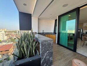 A balcony with a view of the city, a kitchen area with modern appliances, and a dining space with a glass door. - Fabulous Penthouse with Ocean & Mountain Views (Puerto Vallarta)