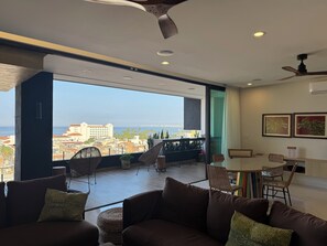 Ein modernes Wohnzimmer mit großem Fenster, Deckenventilator und Essbereich mit Stühlen und Tisch.