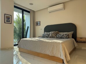 A bedroom with a bed, a nightstand, an air conditioning unit, and a large window with a view of palm trees. - Fabulous Penthouse with Ocean & Mountain Views (Puerto Vallarta)
