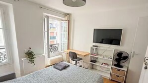 A bedroom with a bed, a desk, a chair, a television, and a radiator. - Cozy studio in the heart of Paris - Eiffel Tower (Paris)