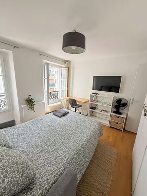 Ein Schlafzimmer mit Bett, Schreibtisch, Stuhl, Fernseher und Heizkörper.