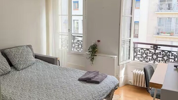 A bedroom with a bed, a desk, a chair, a radiator, and a window with a view of the outside. - Cozy studio in the heart of Paris - Eiffel Tower (Paris)