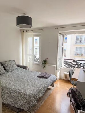 Een slaapkamer met een bed, een bureau, een stoel, een radiator en een raam met uitzicht op het omliggende landschap.