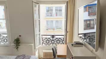 Ein Schlafzimmer mit Bett, Schreibtisch, Stuhl, Heizkörper und einem Fenster mit Blick auf einen Balkon.