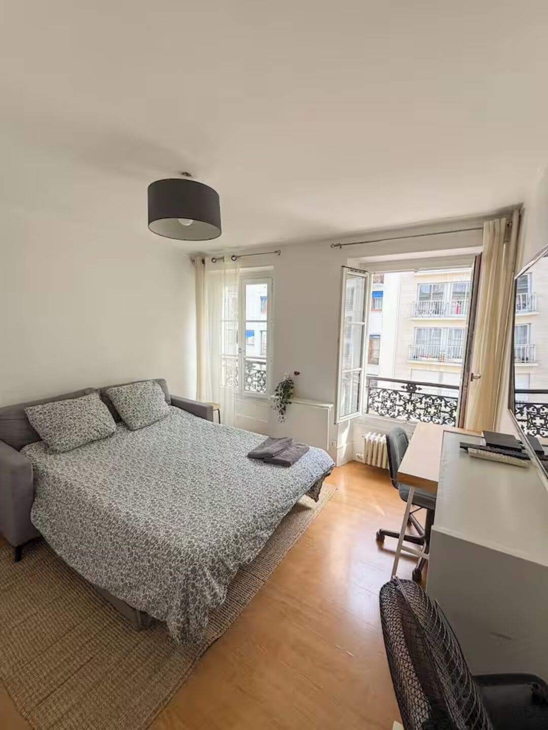 A bedroom with a bed, a desk, and a view of the outside.