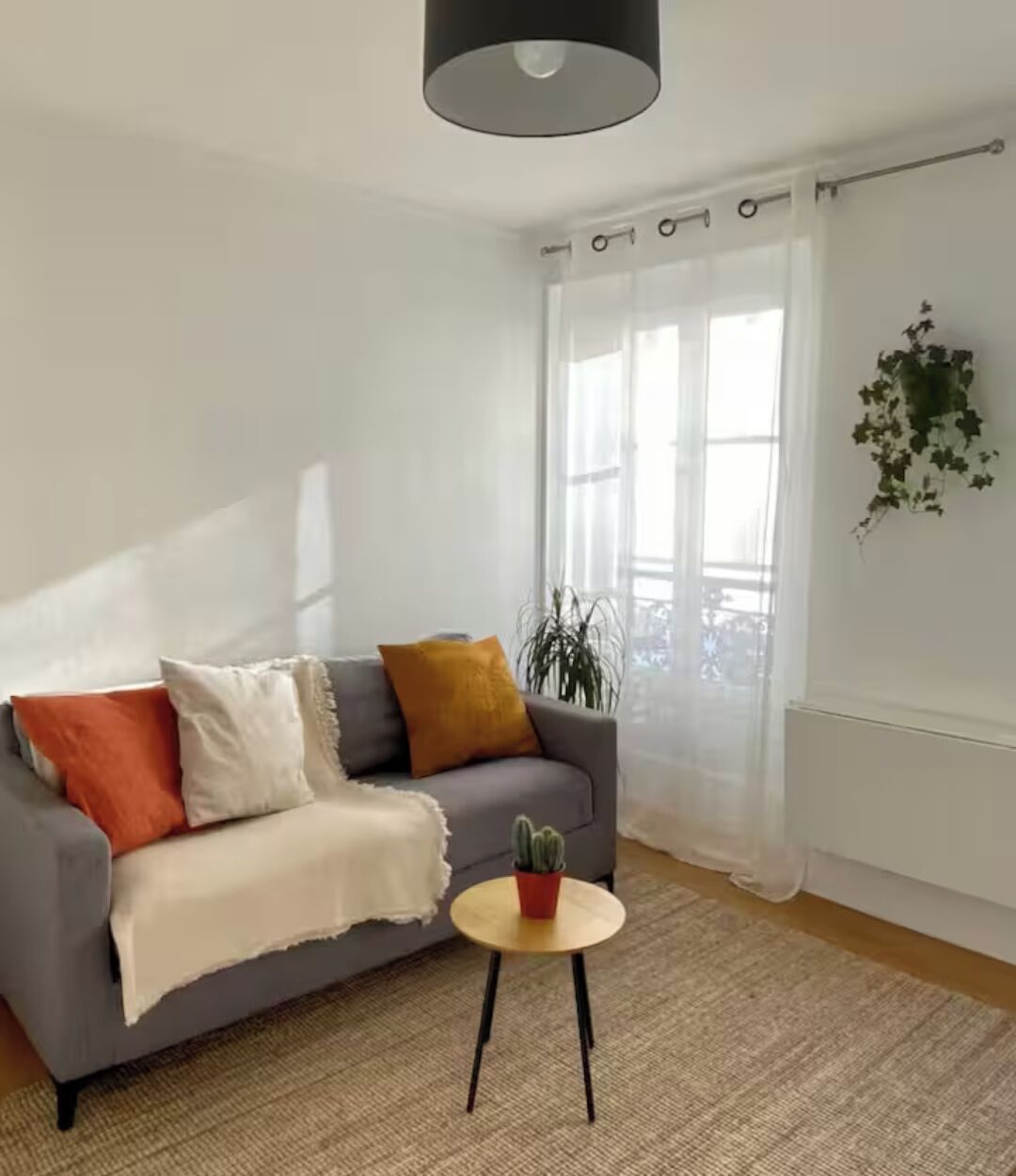 Ein Wohnzimmer mit grauem Sofa, einem kleinen runden Tisch und einem Blumentopf.