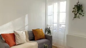 A living room with a grey sofa, a small round table, and a potted plant. - Cozy studio in the heart of Paris - Eiffel Tower (Paris)