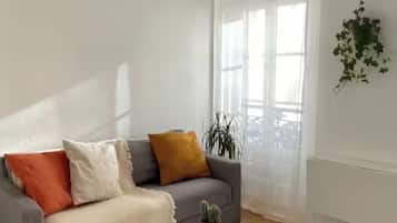 Ein Wohnzimmer mit grauem Sofa, einem kleinen runden Tisch und einem Blumentopf.