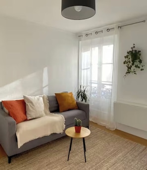 Ein Wohnzimmer mit grauem Sofa, einem kleinen runden Tisch und einem Blumentopf.