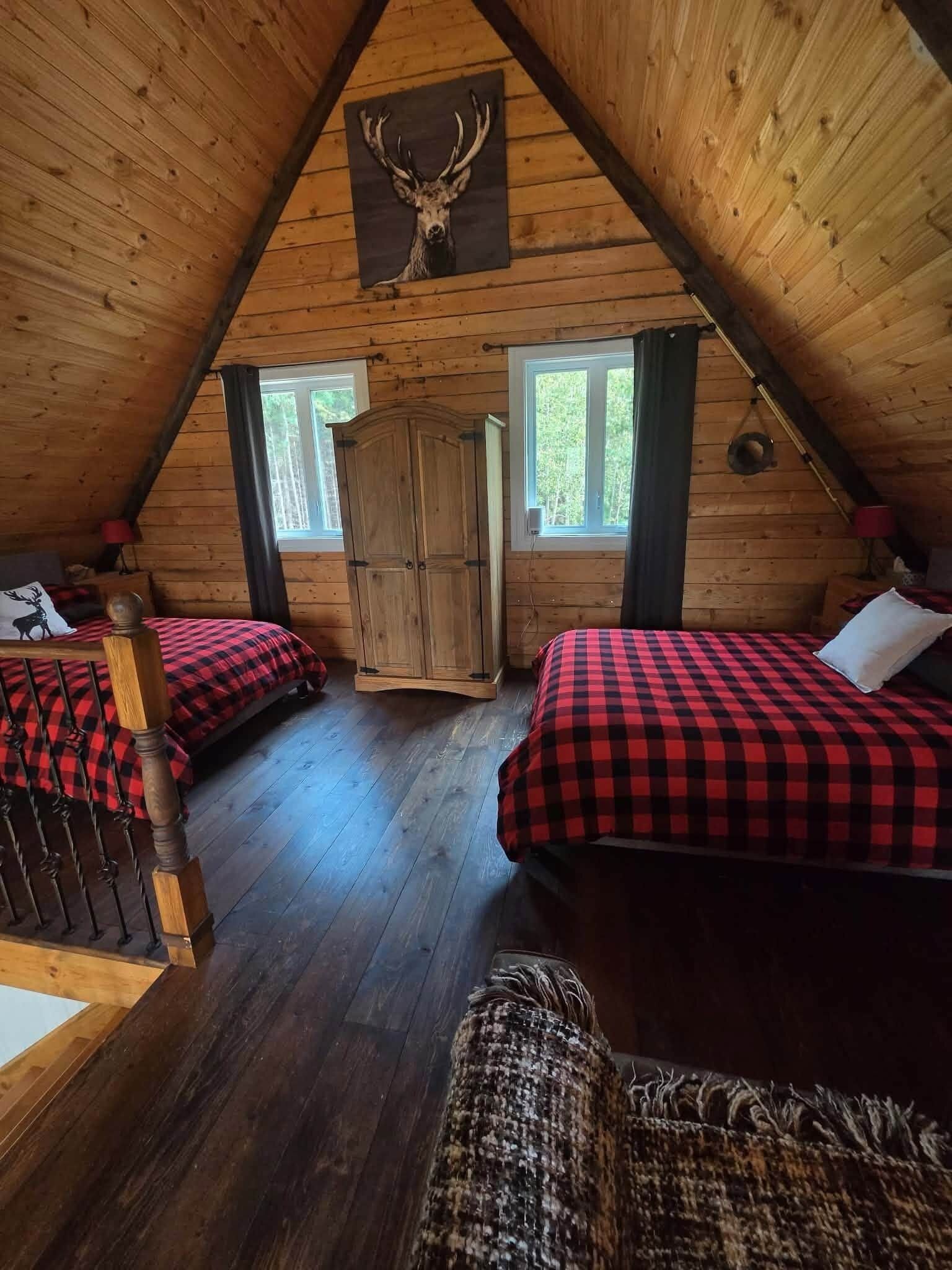 Mökki, jossa on kalteva katto, kaksi sängyä ruutukuosisilla vuodevaatteilla, puinen vaatekaappi ja seinälle kiinnitetty peuranpää.