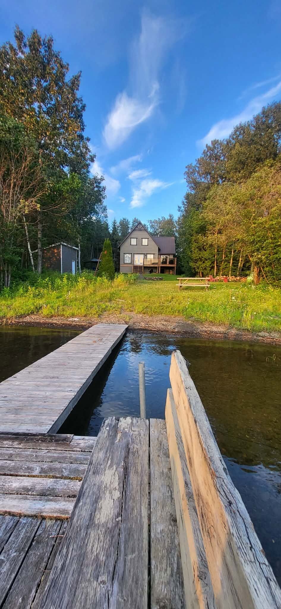 Puinen laituri, joka ulottuu tyynen vesialueen päälle, ja taustalla näkyy puilla ympäröity talo.