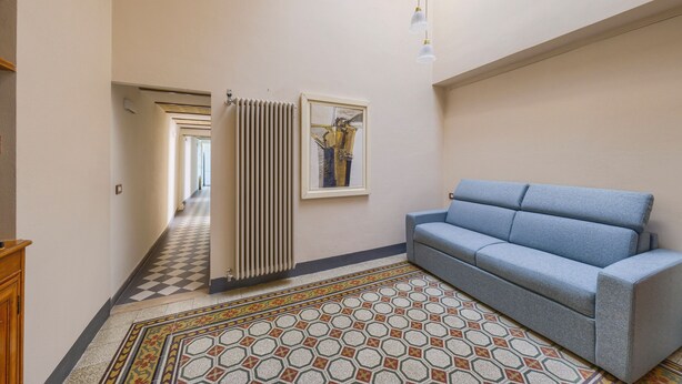 A hallway with a radiator, a blue sofa, and a patterned rug. - The Grammar Teacher's House - Historic Residence (Prato)