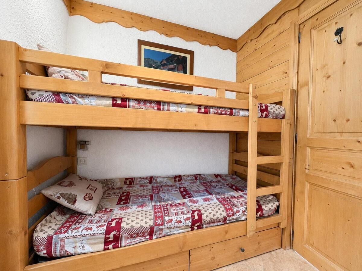 Un lit superposé avec une couvre-lit à motifs, une tête de lit en bois et un petit tableau encadré au-dessus.