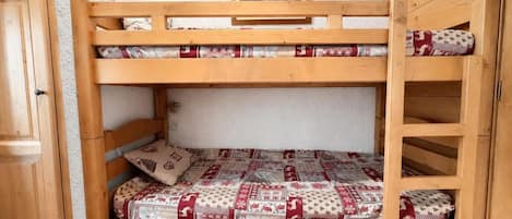 A bunk bed with a wooden frame, a quilted mattress, and a pillow with a patterned design.