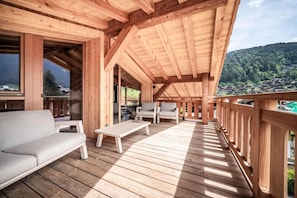Eine Holzterrasse mit einer Couch und Sesseln, mit Blick auf eine gebirgige Landschaft.