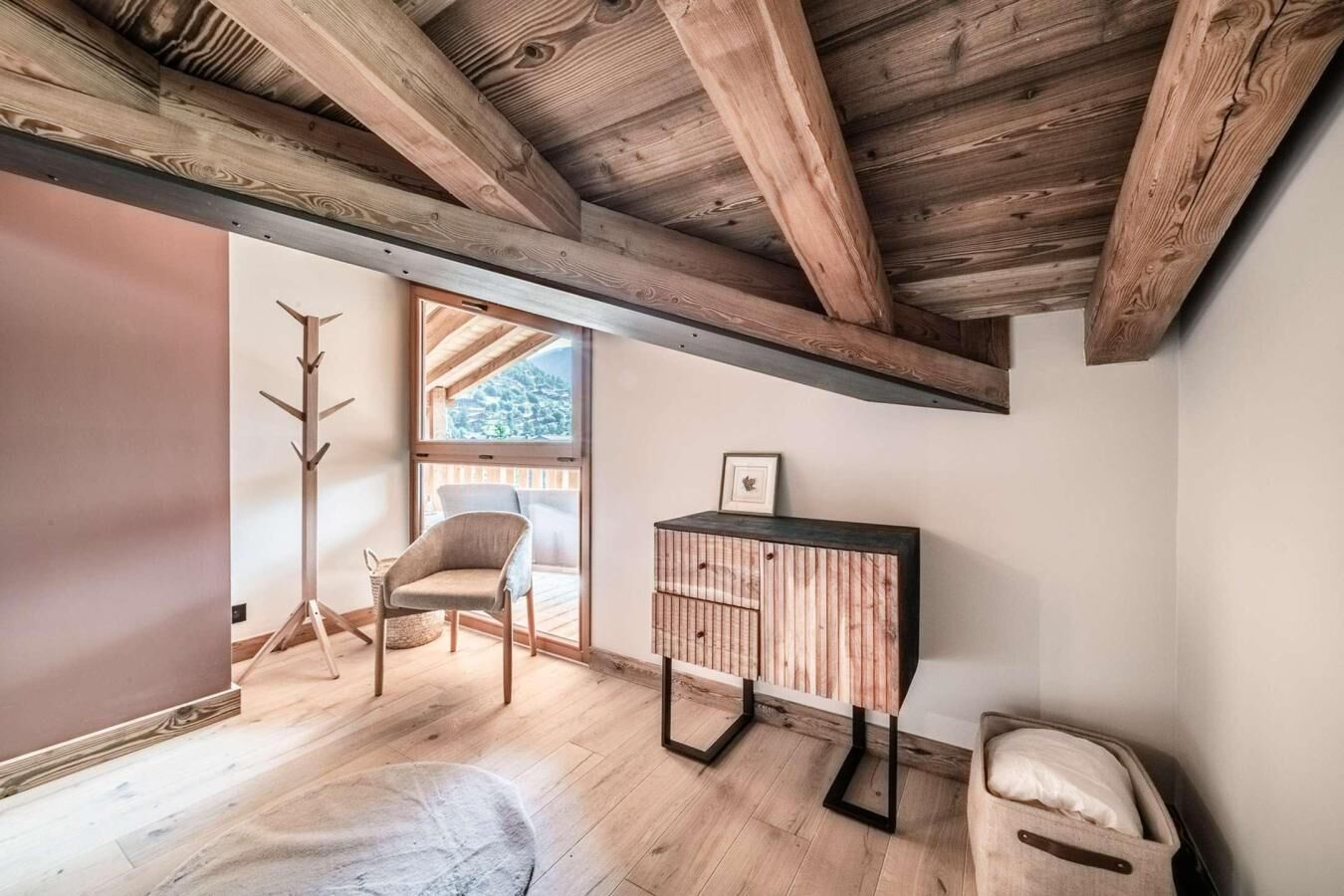 A room with wooden beams, a coat rack, a chair, a small table, and a suitcase.