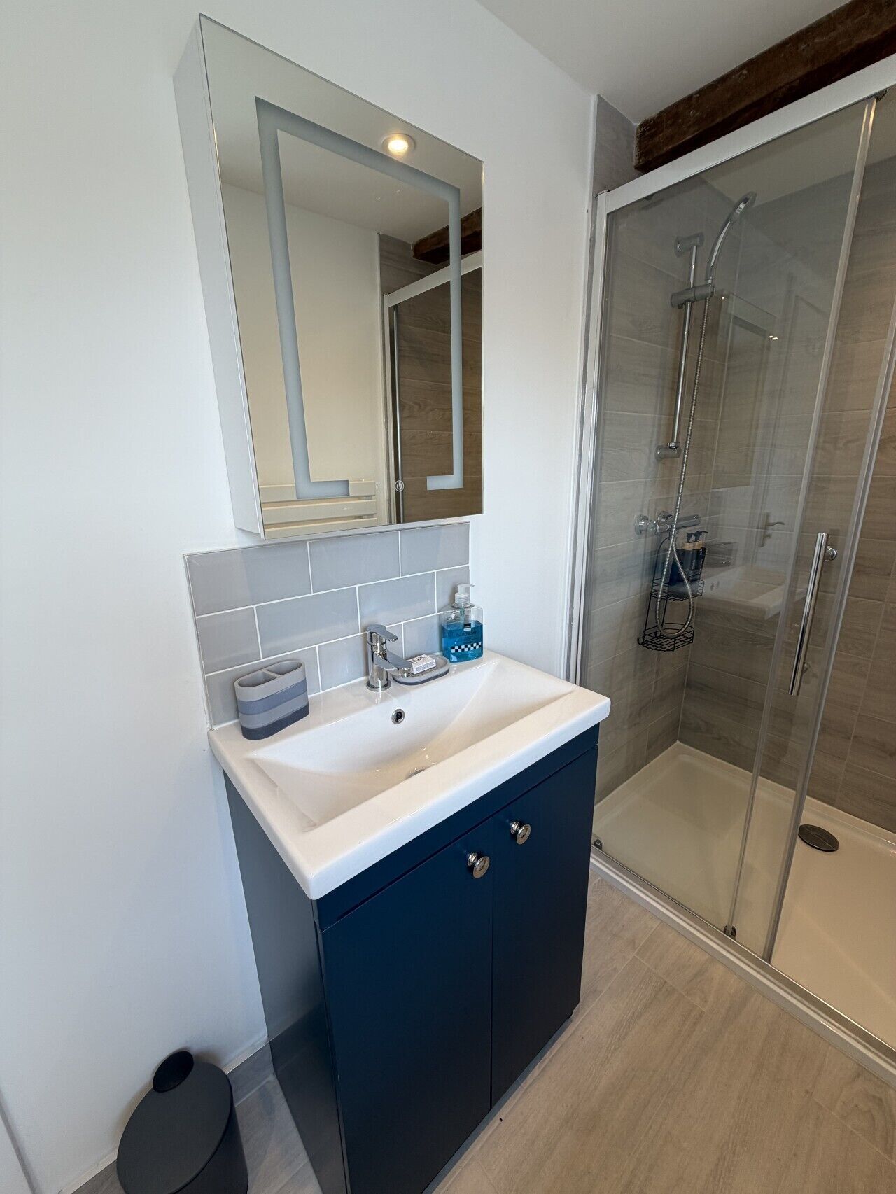 Une salle de bain moderne avec un lavabo blanc, un meuble bleu foncé et une cabine de douche en verre.