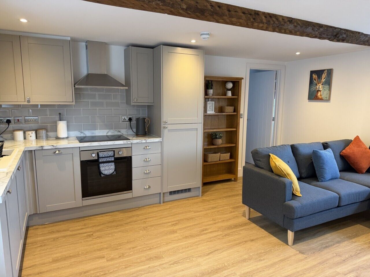 A modern kitchen with grey cabinets, a built-in oven, and a wooden floor.
