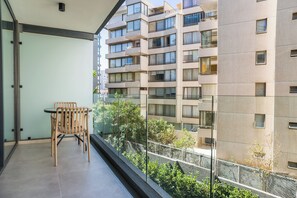 A balcony with a table and chairs, overlooking a modern apartment building with multiple balconies. - Chic Apartment in Las Condes (Las Condes)