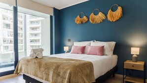Une chambre à coucher avec un lit, des tables de chevet, une fenêtre et une vue sur un immeuble.
