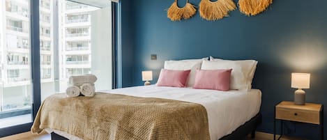 A bedroom with a bed, bedside tables, a window, and a view of a building.