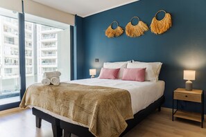 A bedroom with a bed, bedside tables, a window, and a view of a building. - Chic Apartment in Las Condes (Las Condes)