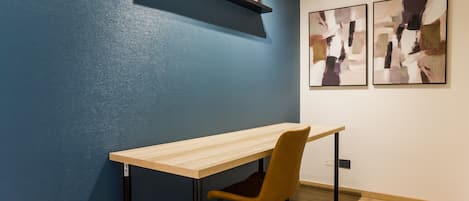 A room with a desk, chair, and two framed artworks on the wall.