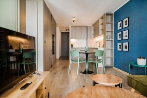 Una cocina moderna con armarios blancos, un comedor con una mesa redonda y sillas, y una pared de acento azul con cuadros enmarcados.