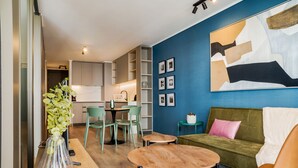 Un salon moderne avec un canapé, une table basse et des fauteuils. On y trouve également un coin repas avec une table et des chaises. Le mur d’accent est bleu et la pièce est agrémentée d’un grand tableau abstrait.