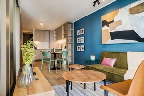 A modern living room with a sofa, coffee table, and chairs. There is a dining area with a table and chairs. The room has a blue accent wall and a large abstract painting. - Chic Apartment in Las Condes (Las Condes)