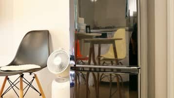 A compact living space with a modern black refrigerator, a small white fan, a wooden chair, and a table with chairs.