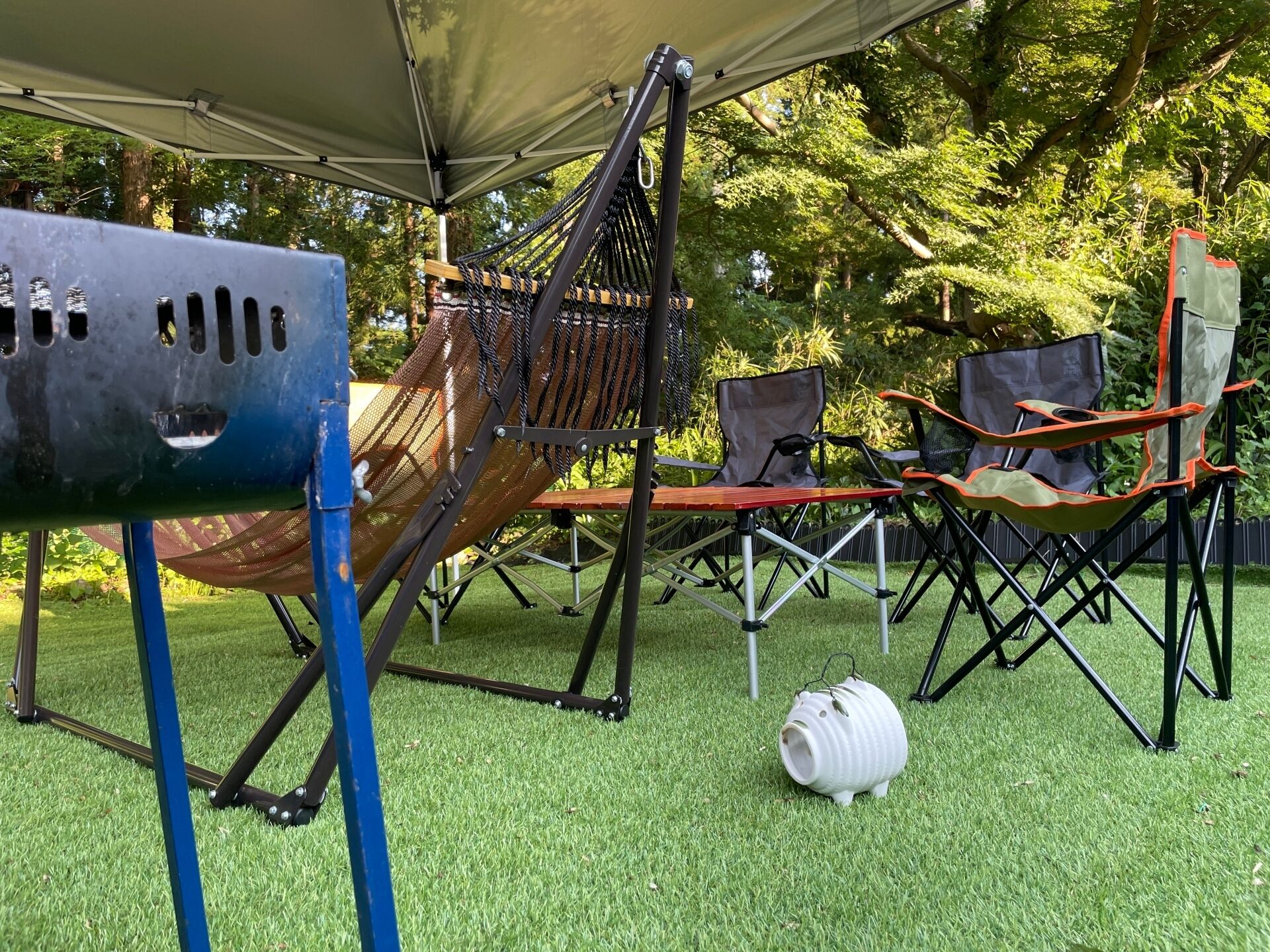 Ein Außenbereich mit einer Hängematte, einem Grill und Campingstühlen.