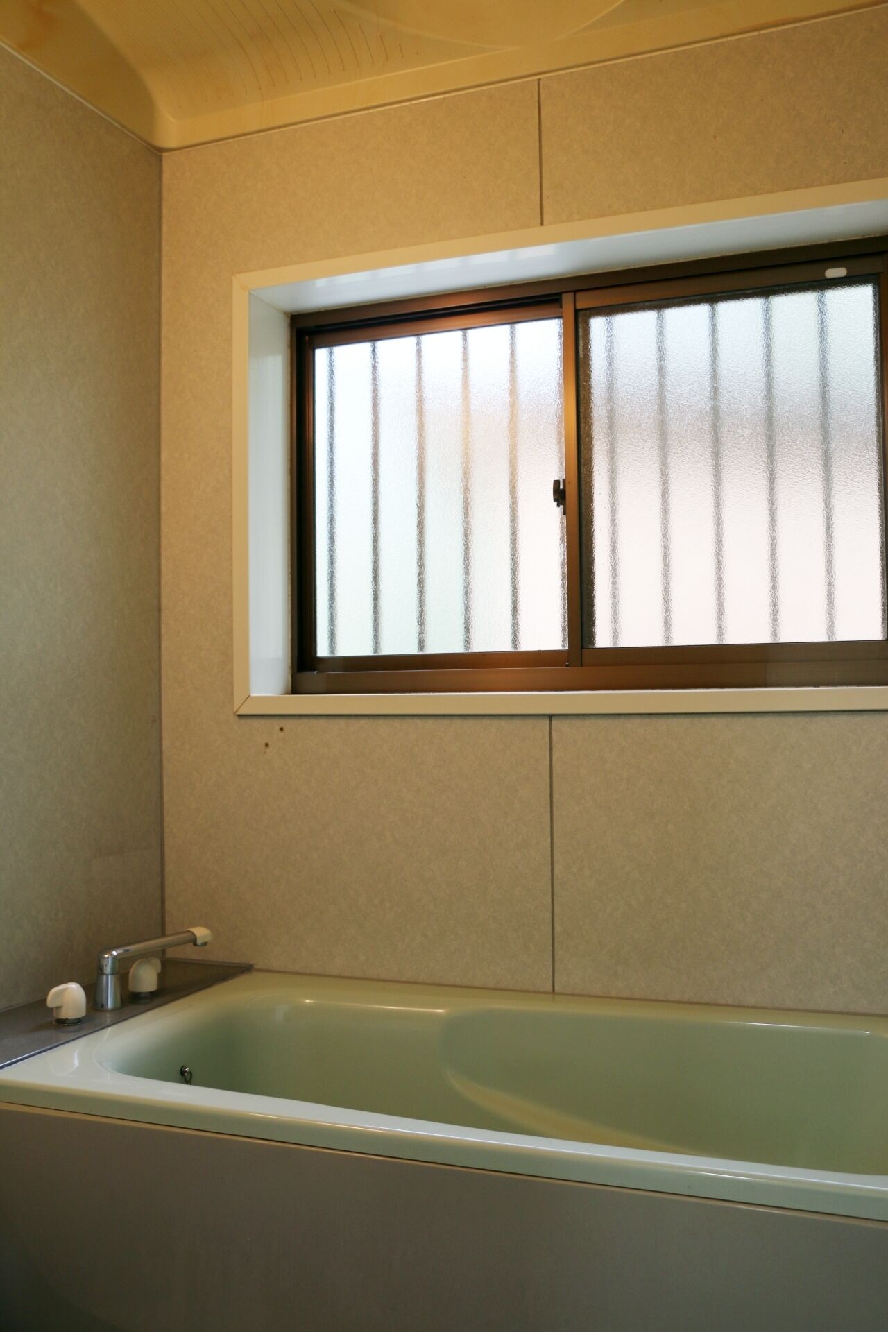 Une salle de bain avec une baignoire, une fenêtre à carreaux dépolis et un porte-serviettes.