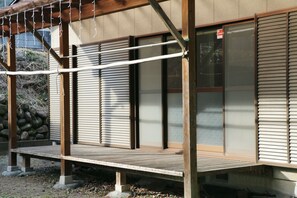 A traditional Japanese building with a wooden deck, sliding doors, and a stone wall in the background.