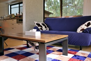 Una habitación con una mesa de madera, un sofá azul con almohadones de cuero de vaca y un tapete a cuadros.