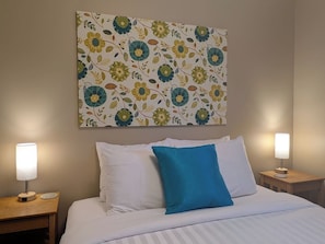 A hotel room with a bed, two bedside tables, and a wall-mounted artwork.