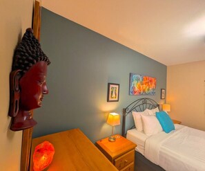 Une chambre à coucher comprenant un lit, des tables de chevet, une sculpture de tête de Bouddha fixée au mur et un tableau.