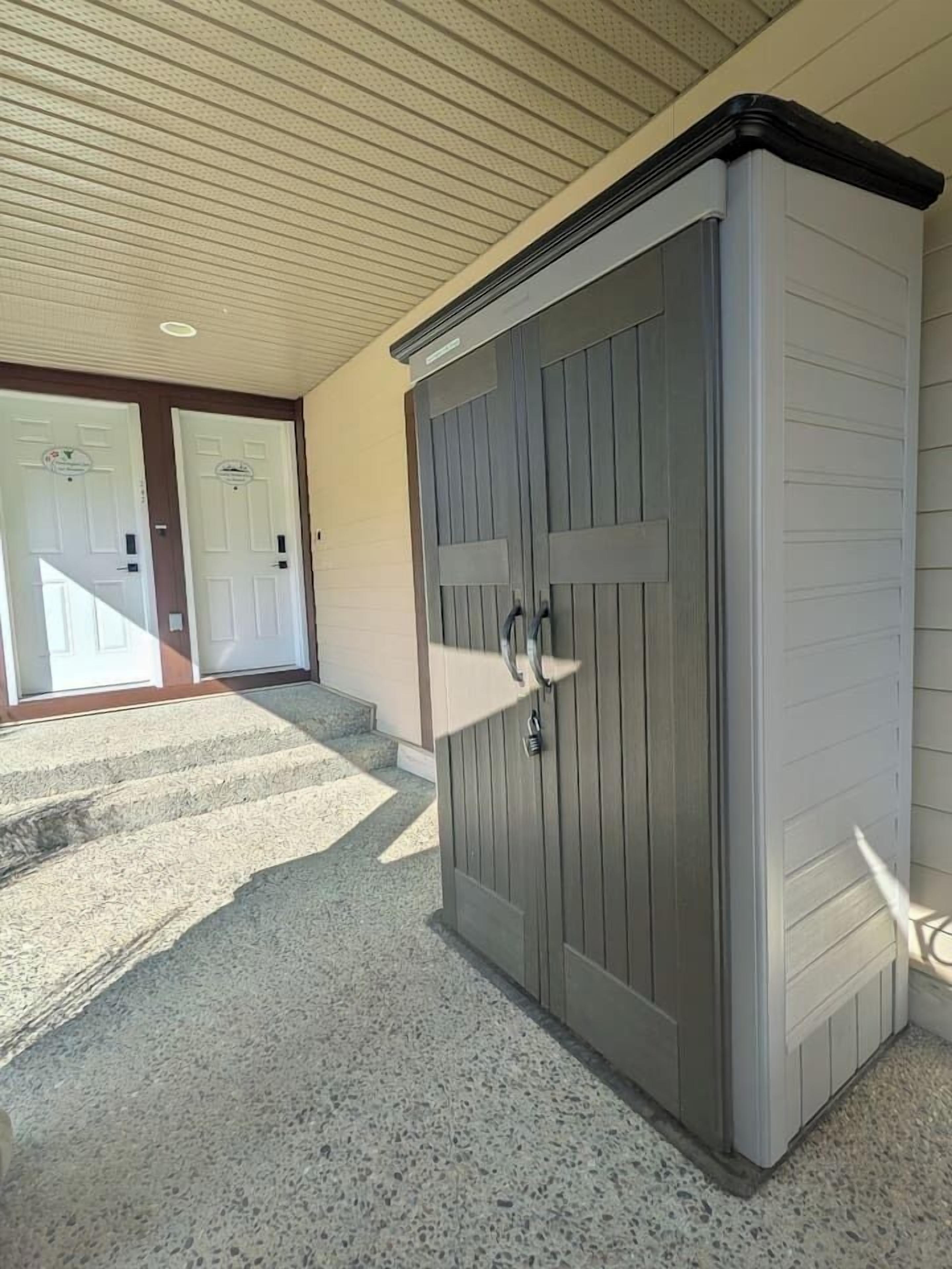 L’entrée d’un immeuble se compose d’une porte grise, d’un petit espace formant un porche et d’un escalier menant à une porte blanche.